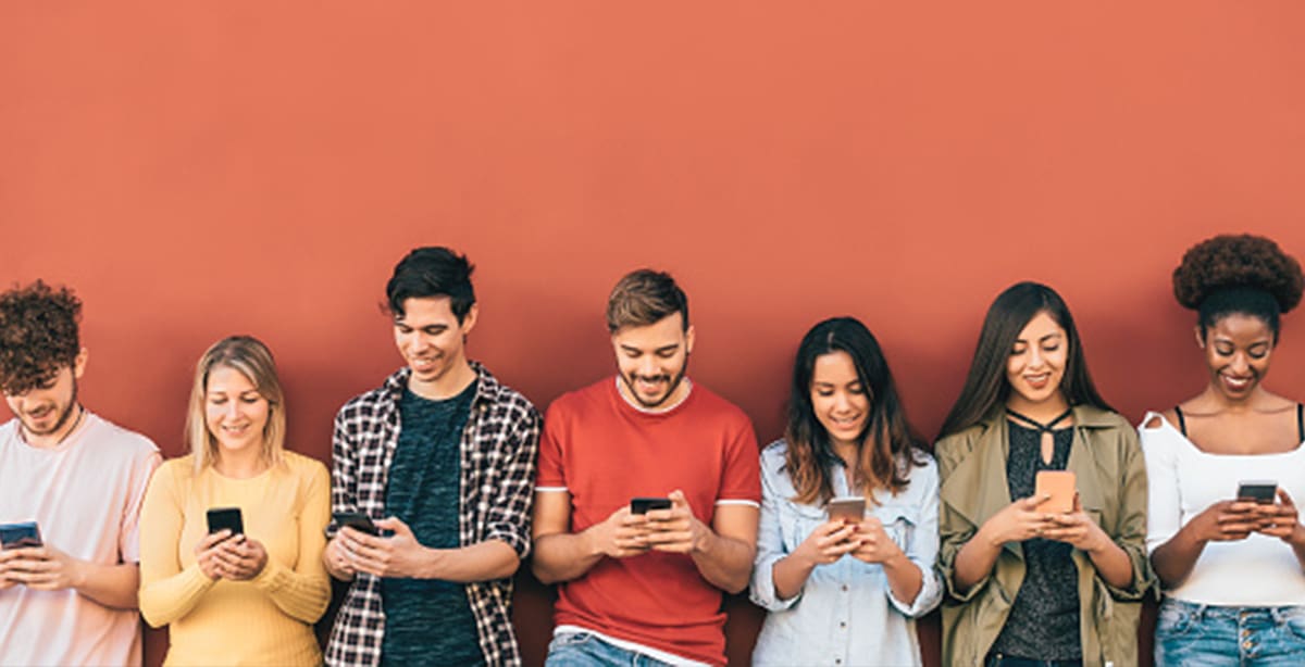 People standing against a wall, everyone on their phones